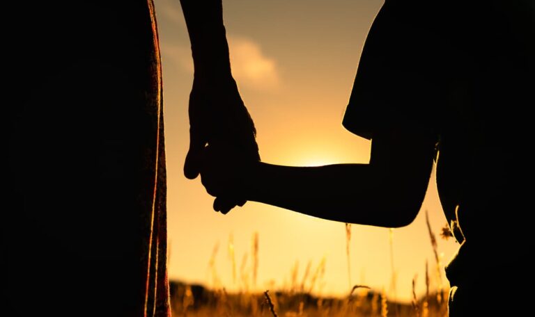 Silhuett av en vuxen och ett barn som håller varandra i handen vid solnedgången, vilket symboliserar adoption och juridisk trygghet. Bilden representerar vikten av Apostille på adoptionsdokument för att säkerställa giltighet i internationella adoptionsprocesser.