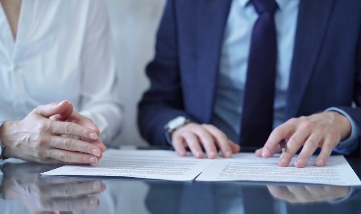 Två personer i formell klädsel granskar och signerar viktiga juridiska dokument vid ett bord, vilket symboliserar vikten av auktoriserad översättning för internationella och juridiska ändamål. Perfekt bild för blogginlägget om varför auktoriserade översättningar är avgörande vid legalisering och affärstransaktioner på Apostille24.se