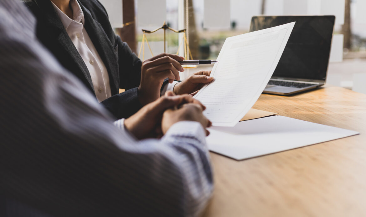 Två personer i formell klädsel granskar och diskuterar en juridisk fullmakt vid ett kontorsbord, med en våg av rättvisa i bakgrunden som symboliserar juridisk legitimitet. Bilden representerar vikten av korrekt utfärdade fullmakter och Notarius Publicus roll i att verifiera och legalisera dokument.
