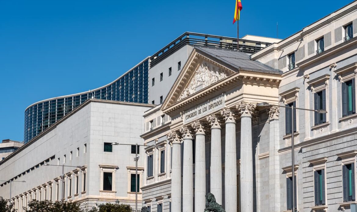 Fasad av Spaniens parlament "Congreso de los Diputados" i Madrid, med spanska flaggan vajande på taket – en symbolisk plats för juridiska och administrativa ärenden som NIE-nummer och legalisering av dokument.